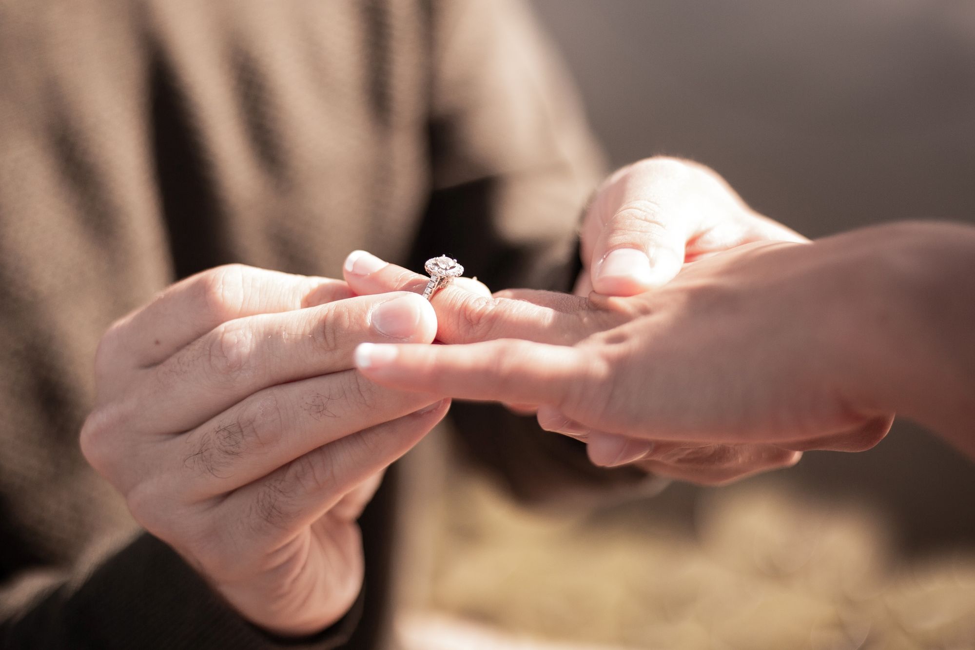 A close cropped photo of a man sliding an engagement ring onto his partners ring finger.