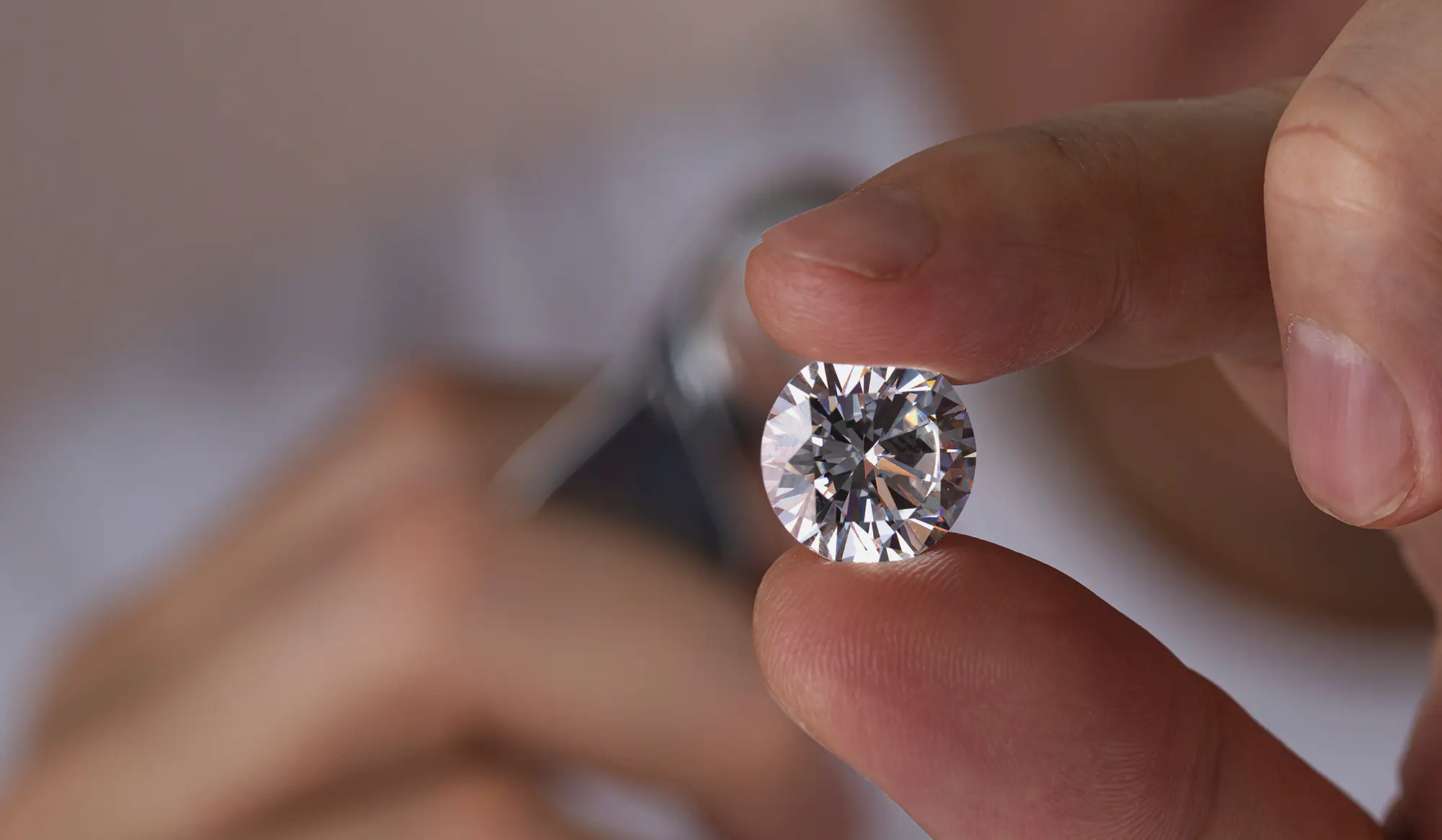 Person holding a large round brilliant cut diamond, inspecting it through a jewelers magnifying loupe.