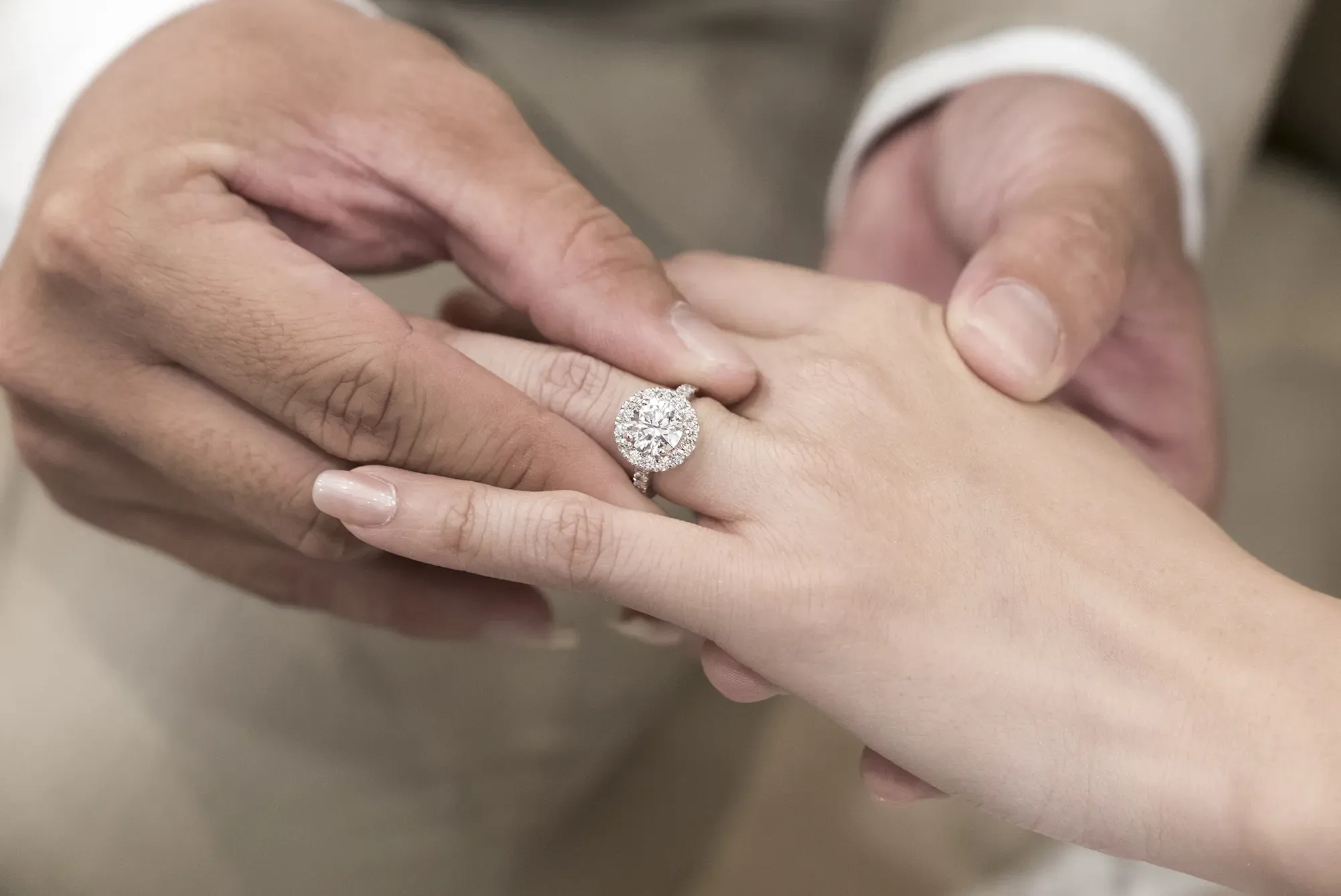 Close up of an engaged couples' hands. The man is putting a beautiful diamond ring onto the woman's ring finger.