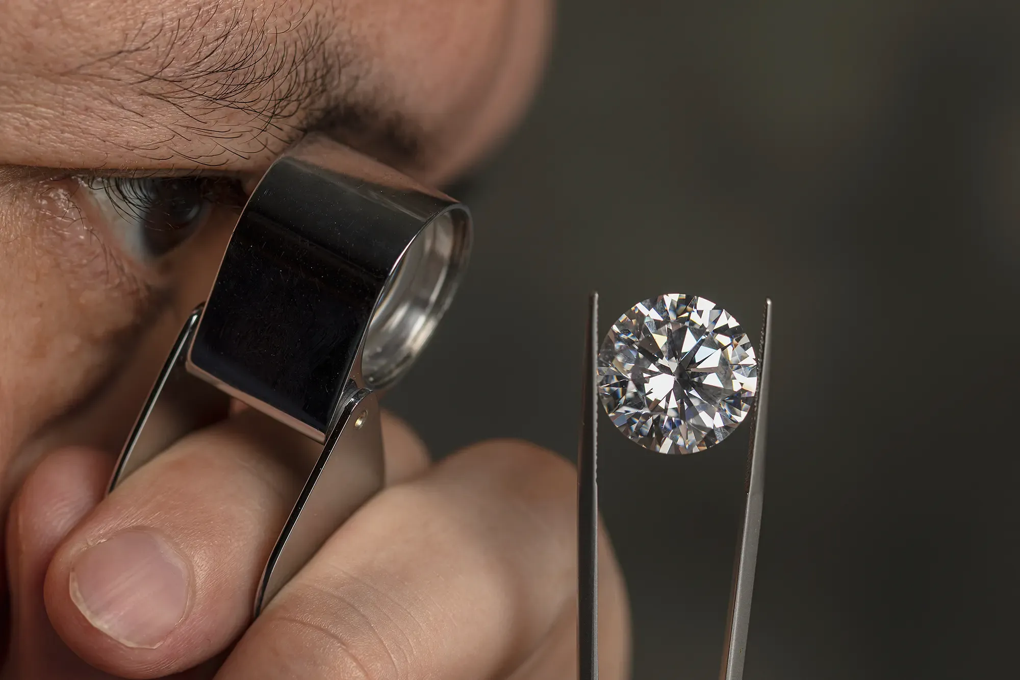 Close up of a man inspecting a large round brilliant diamond through a jewelers loupe.