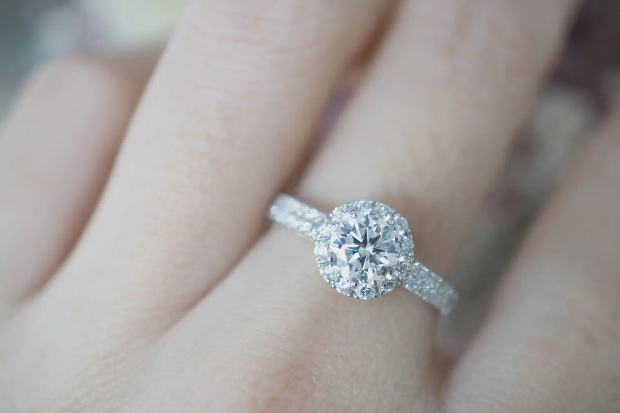 White gold engagement ring on a woman's finger. The ring is a halo-set round brilliant diamond with diamonds around the band.