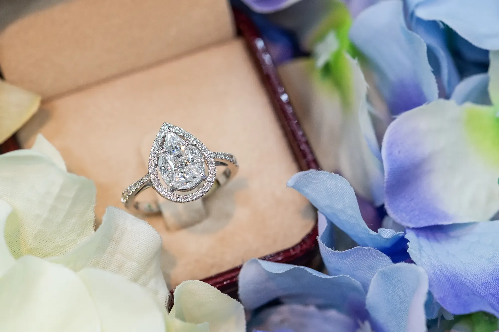 Diamond engagement ring with a large pear shaped diamond. The ring is in a ring box, surrounded by flowers.