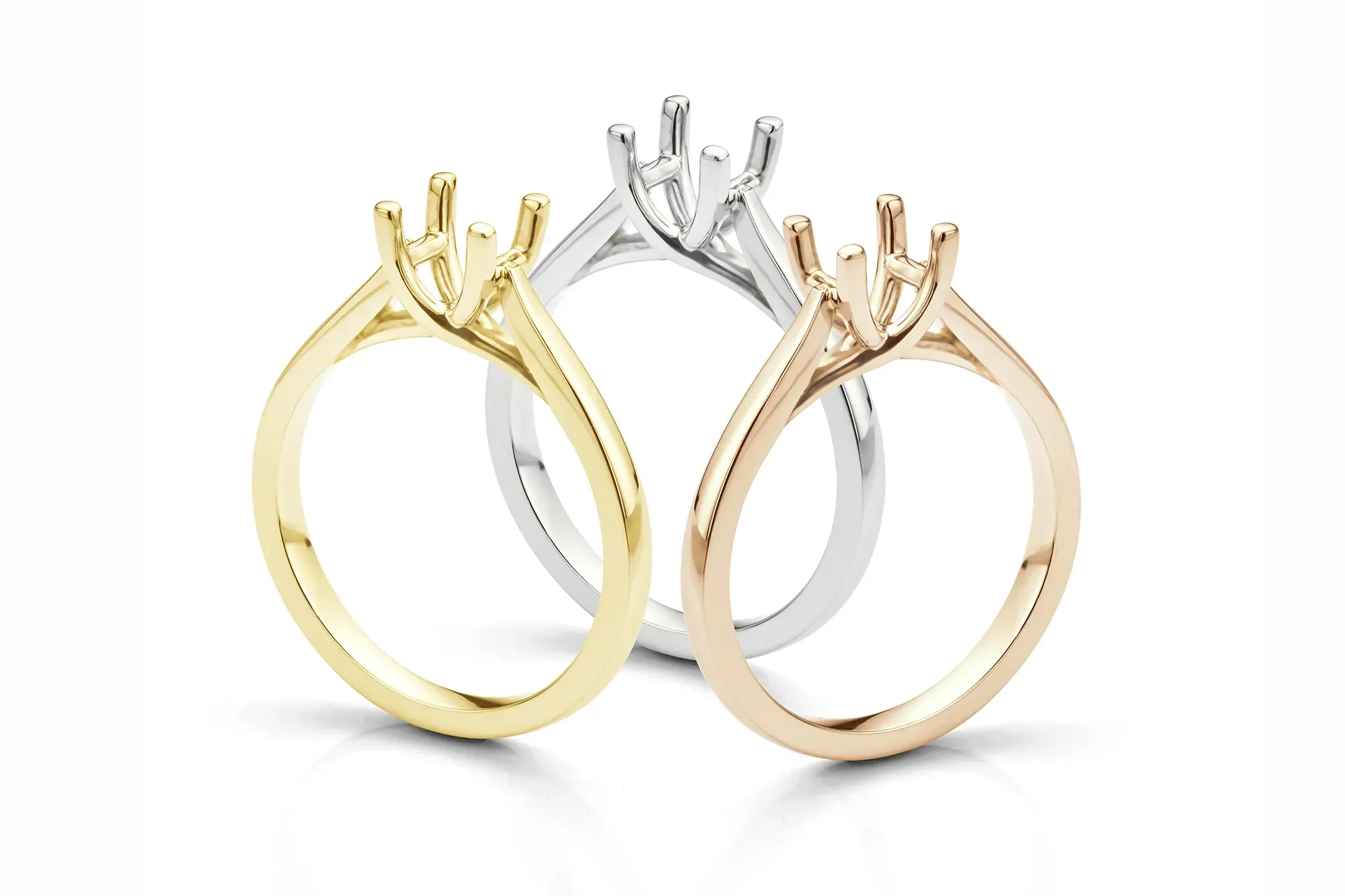 Three solitaire ring settings, without their diamonds yet. One ring setting is yellow gold, one white gold and one rose gold.