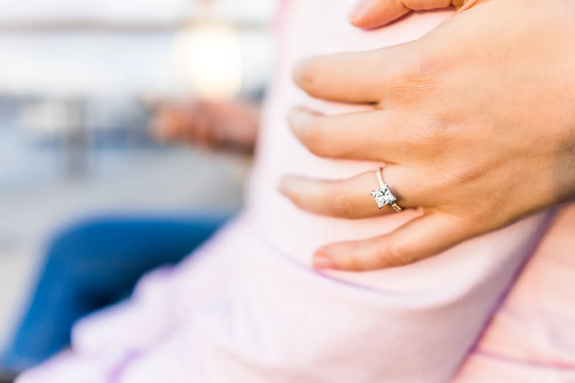 A woman's hand resting lovingly on a man's arm. She is wearing a princess cut diamond engagement ring.