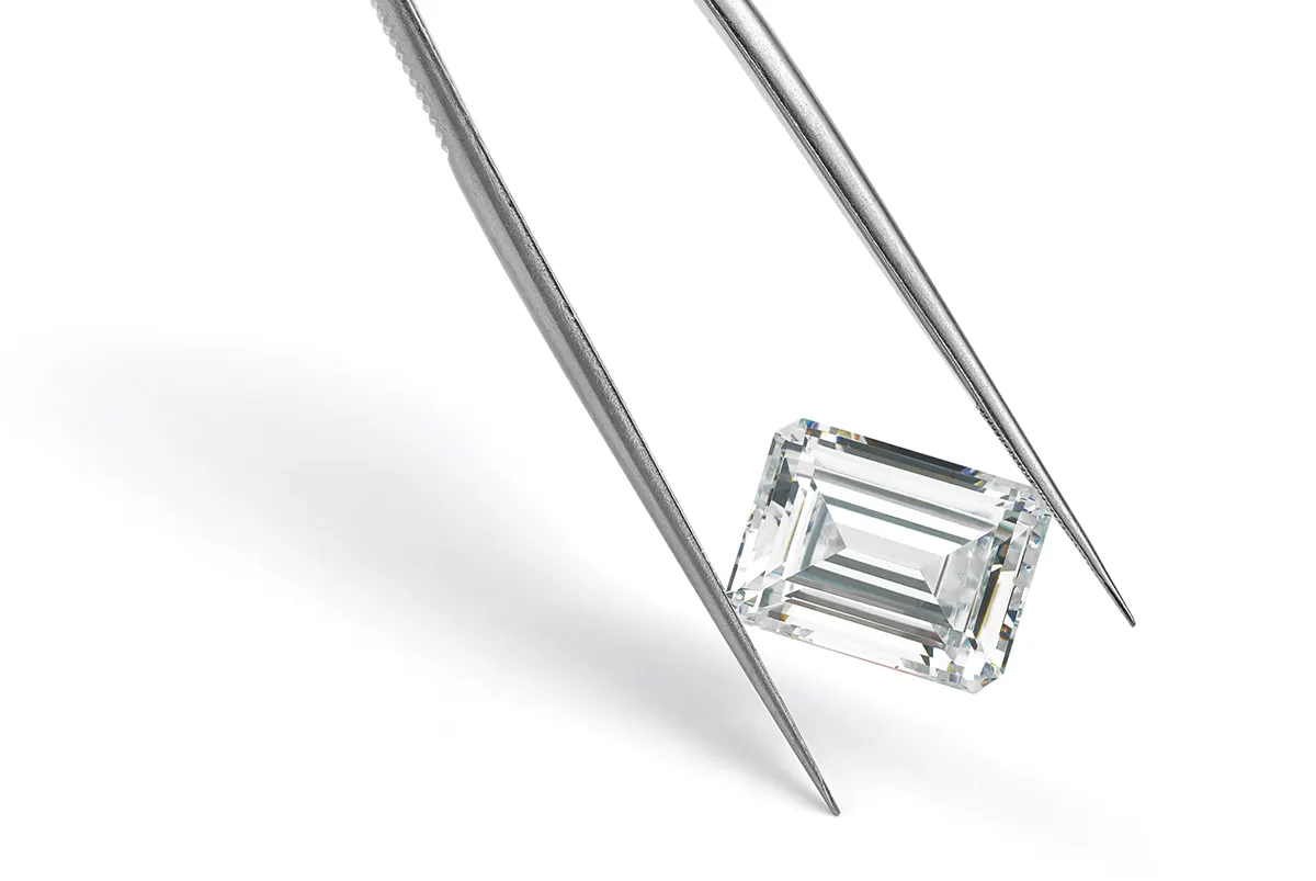 An emerald cut diamond held in tweezers.